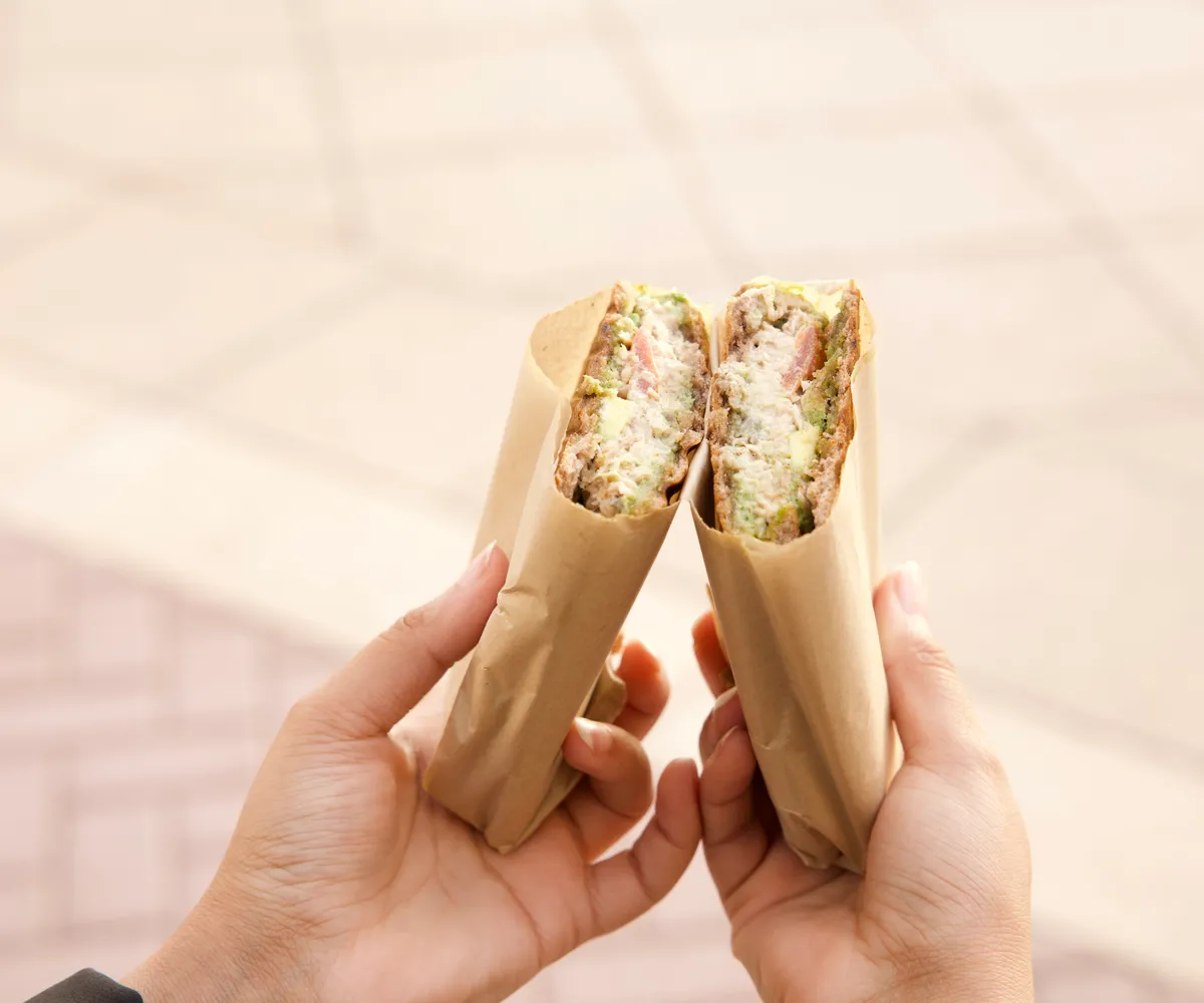 hands holding two halves of a wrapped sandwich